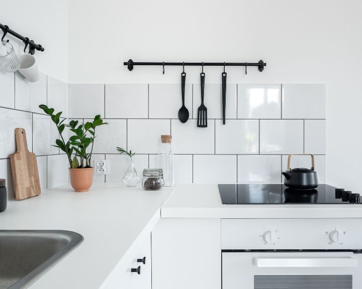 A remodeled kitchen in the city with a stove top, sink and a white tiled background.
